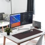Black leather desk pad protecting a wooden desk, with a laptop and mouse on its surface, viewed from above.